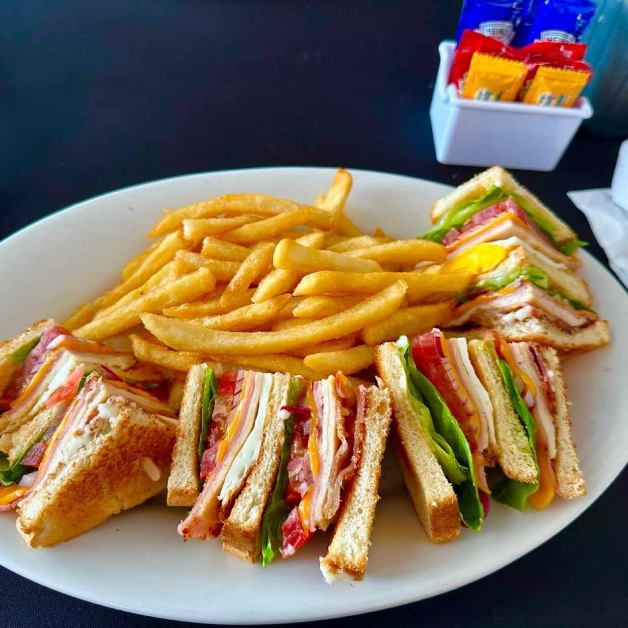 CLUB SÁNDWICH (Tres Capas de Pan Tostado con Jamón, Pavo, Huevo, Tocino, Queso, Lechuga, Tomate y Cebolla, servido con nuestra Mayonesa de la Casa) con Papas Fritas