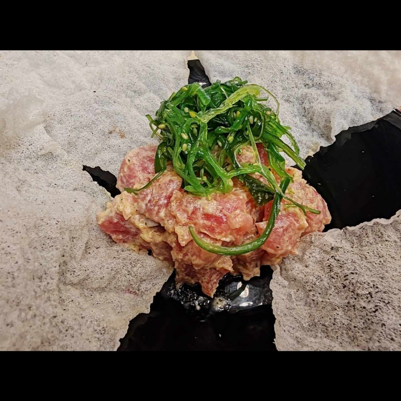 Tartar de atún con mayonesa ligeramente picante, coronado de algas wakame y rodeado de hojuelas de arroz. 