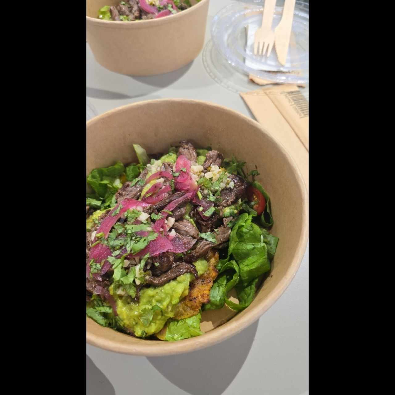 Dos patacones asados con aceite de oliva, cubiertos de guacamole, entraña, chimichurri y cebolla encurtida, sobre ensalada de lechuga y tomate con aderezo de limón