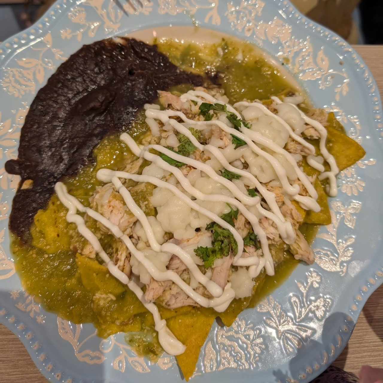 Chilaquiles verdes con pollo mechado, queso mozzarella, crema y frijoles fritos. 