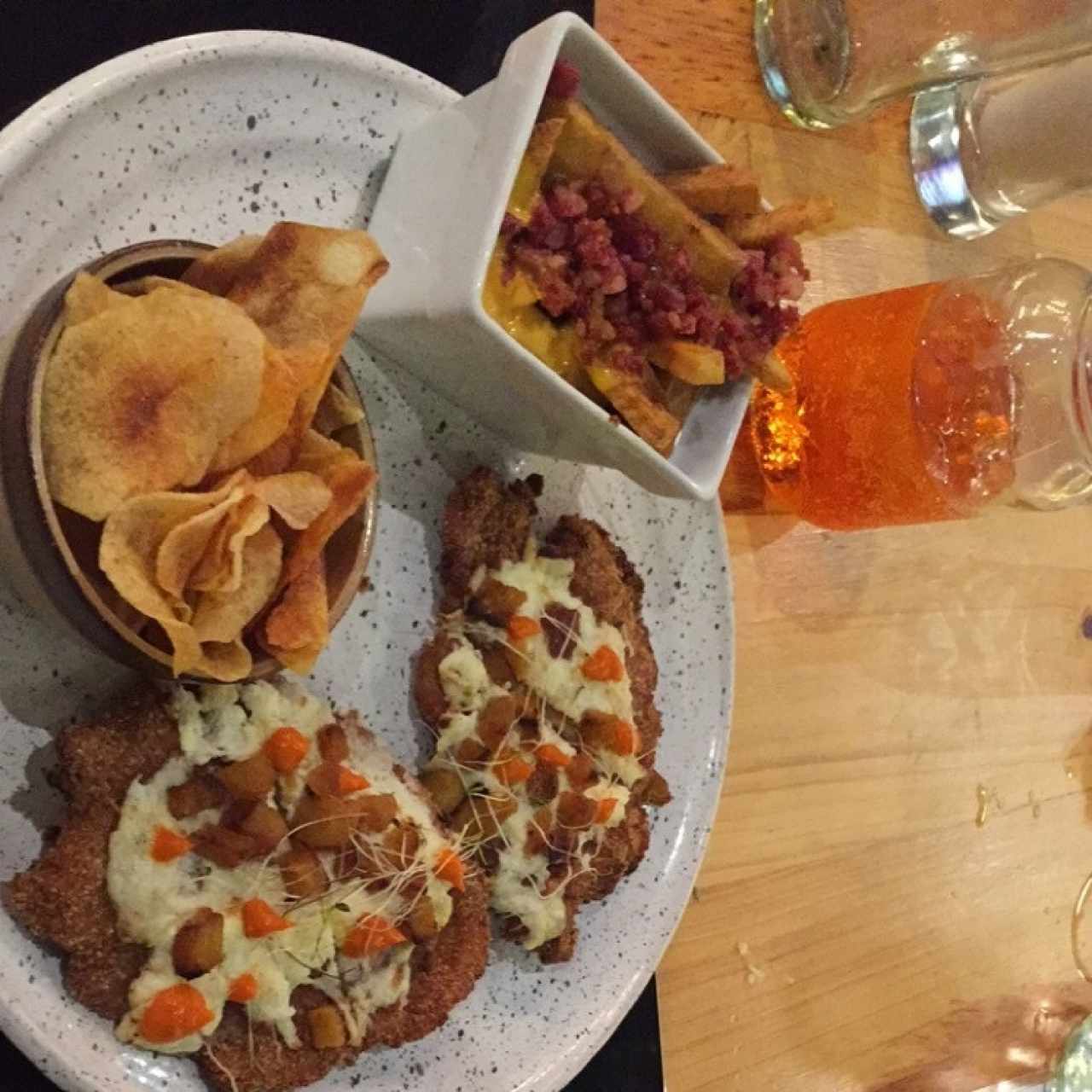 Milanesa de pollo criolla acompañada con papas chips y papas con queso cheddar y tocineta