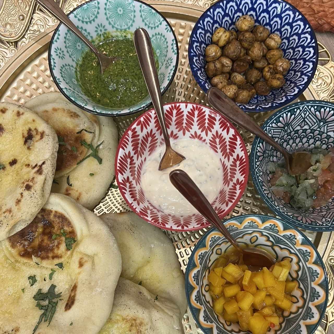 Entrada: pan naan acompañado con raita, ensalada de pepino, garbanzos crujientes, chutney verde y chutney de mango