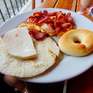 Desayuno sencillo con huevitos y tocino, arepa con quesito y pan de queso.