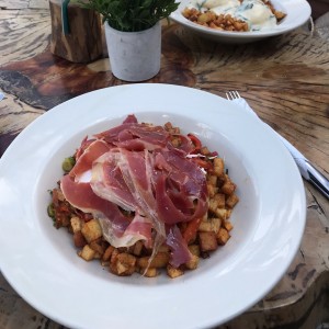 Huevo poche sobre papas con pimiento aceite de oliva y prosciutto. 
