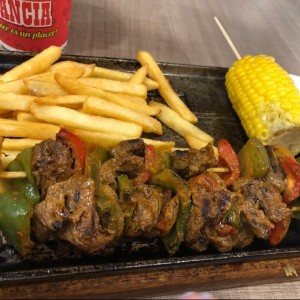 Brochetas de carne de res con mazorca y papas fritas.