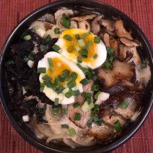 Bossam Ramyun  Sopa de ramyun con puerco (bossam), cebollita, cebolla, hongo enoki, hongo negro, huevo, berro y ajo. 