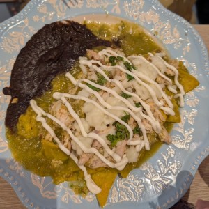 Chilaquiles verdes con pollo mechado, queso mozzarella, crema y frijoles fritos.