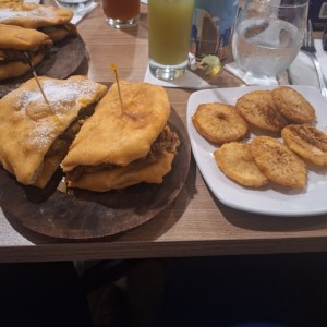 Es una mita de emperedado porkbelly una mitad de emparedado patriota, junto con patacones de yuca y guapo (jugo de caña).