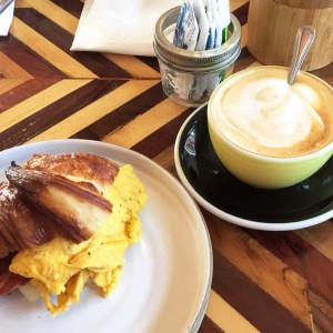delicioso desayuno, corissant con huevo revuelto, tocino y queso. y un capuchino