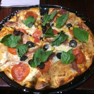 Pizza en masa de oregano, con peperoni, aceitunas negras, maiz, cebolla caramelizada y albahaca.